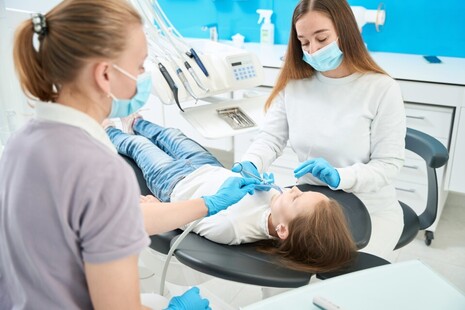 pedodontist giving local anaesthetic injection to girl assisted by nurse