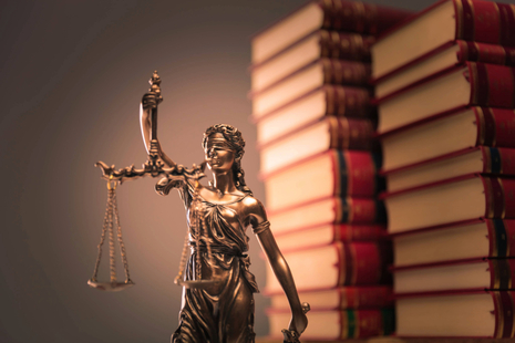 Bronze Lady Justice statue holding scales beside stacked law books against a softly blurred background.