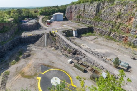Large pit with a dirt track and yellow painted circle at the front and white building towards the back
