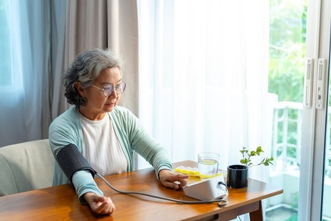 Older woman sits checks her blood pressure using machine. Credit: iStock Photo
