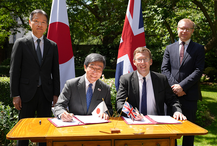 Four men, two sitting and two standing, around a table signing a document