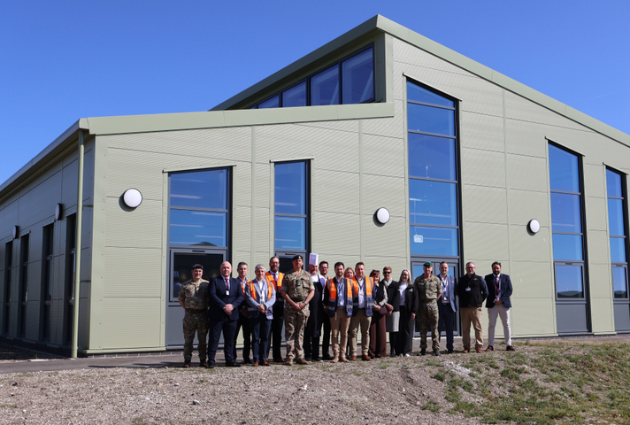 A group of civilian and military people are standing in front of a new building