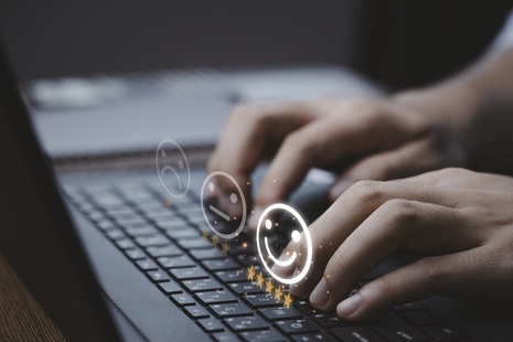 Person typing on laptop with smiley faces floating over the keyboard. Credit: iStock Photo