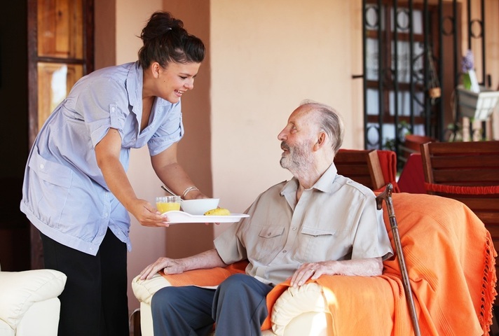 Nurse hands food tray to older man in chair. Credit: Shutterstock
