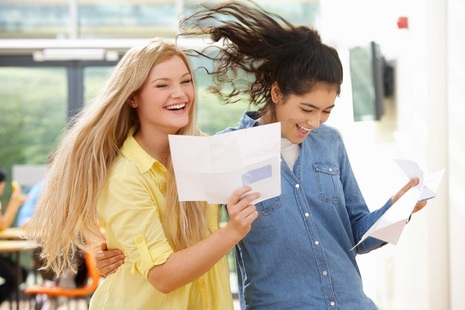 Two female students looking happy, holding pieces of paper.