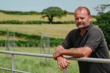 Farmer Lee Pedley leaning on a gate with his farm in the background.