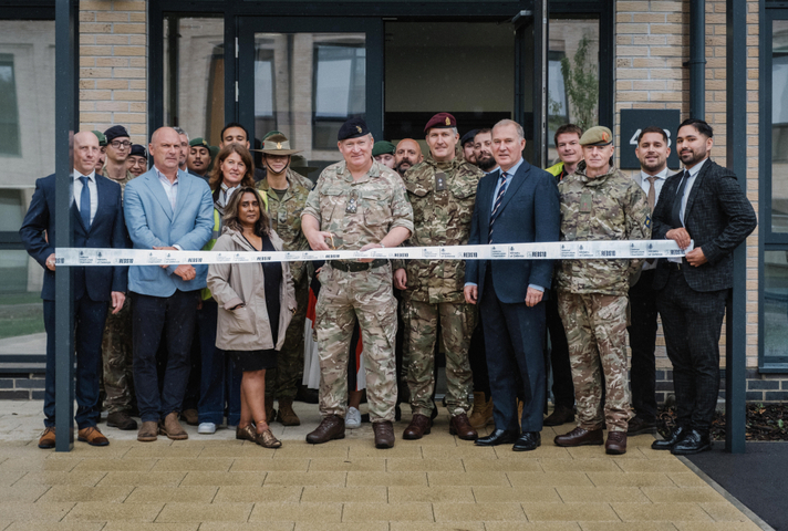 Brigadier Grant Kerr prepares to cut a white ribbon in front of a new building, surrounded by colleagues in a mix of civilian clothes and Army uniforms.