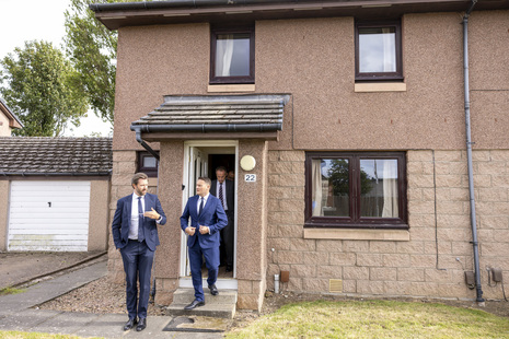Three men in suits leave a brown house