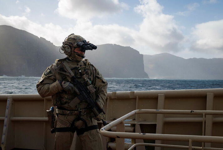A soldier in uniform is pictured at sea against the backdrop of cliffs.