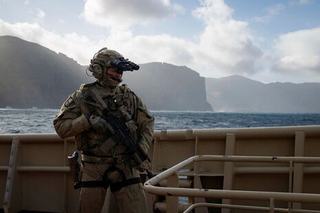 A soldier in uniform is pictured at sea against the backdrop of cliffs.