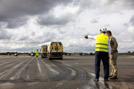 An RAF officer in camouflage uniform listens to a member of the project team, wearing a high vis vest, as he points at something on the runway.