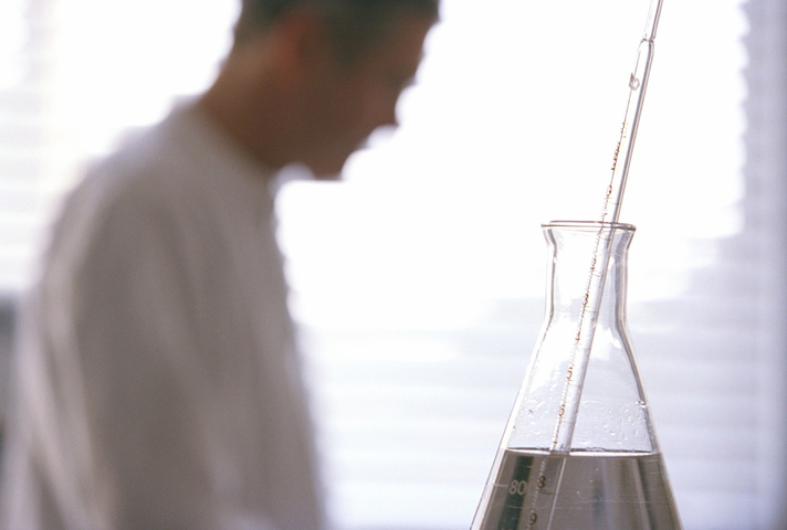 A male scientist tends to a glass laboratory bottle containing a thermometer in a liquid substance.