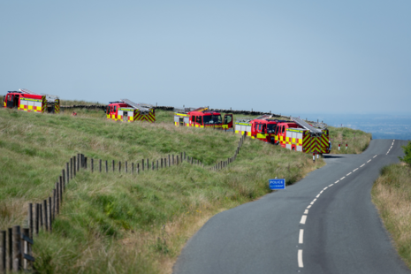 Four fire engines drive in a line down a country lane 