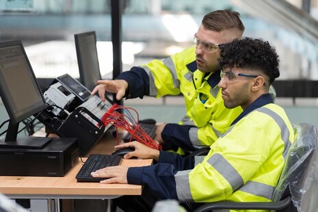 A student wearing a high-vis jacket with a supervisor